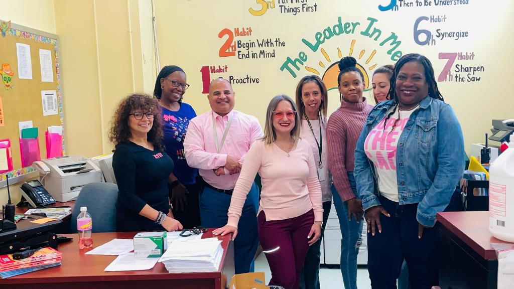 Teachers, administrators pose in the school office wearing pink