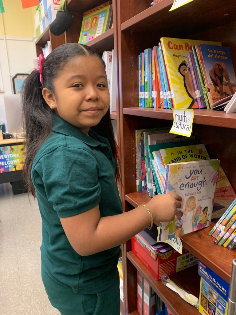 A student is picking up a book from the shelf titled You Are Enough