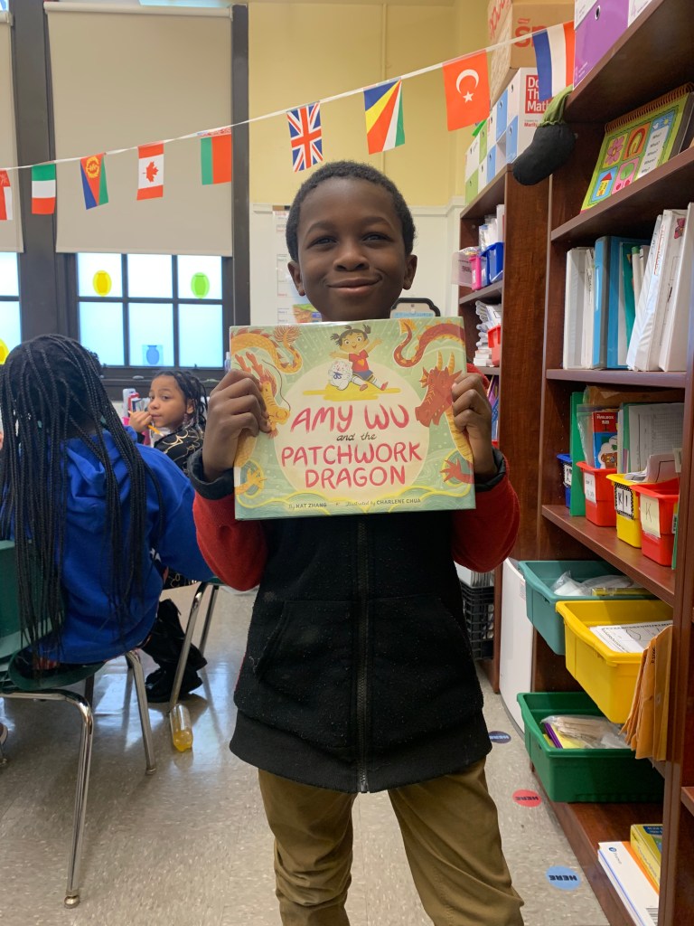 A student is smiling and holding the book by Amy Wu titled Patchwork Dragon