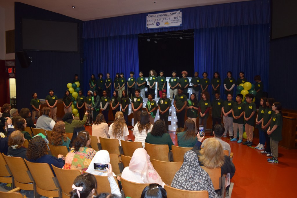 A group of 5th grade students stand on stage, performing "This Is Us," a song inspired by the melody of "This Is Me" from The Greatest Showman.
